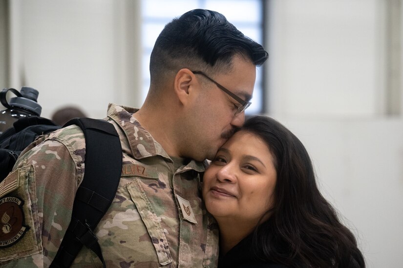 A U.S. Air Force Airman kisses the head of his wife while she looks to the camera