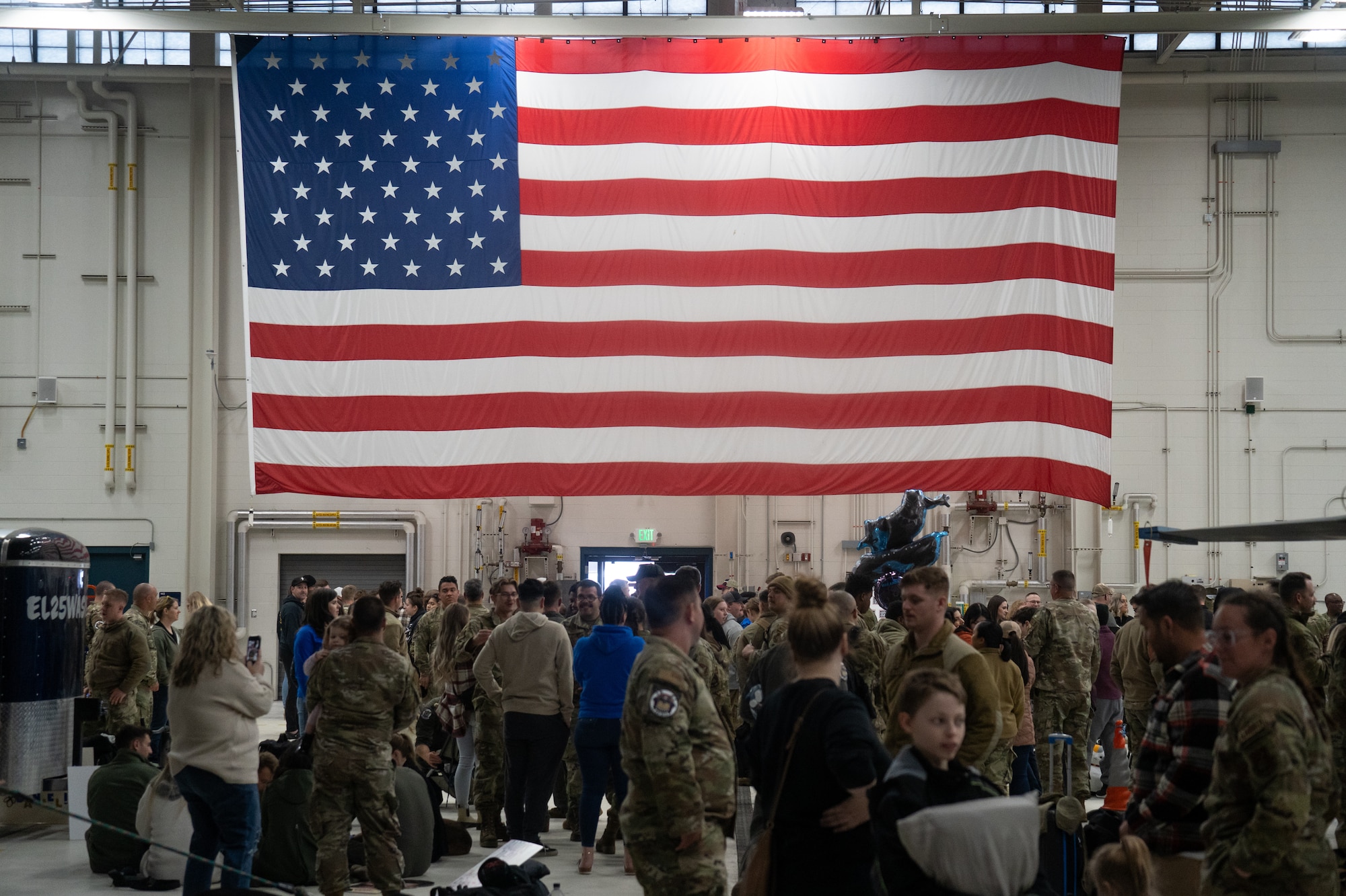 The American flag hangs inside a hanger above a crowd of Airmen, friends, and family members