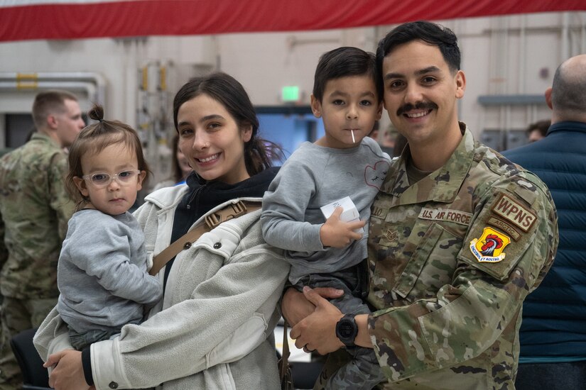 A U.S. Air Force Airman holds his son, next to his wife holding their daughter.