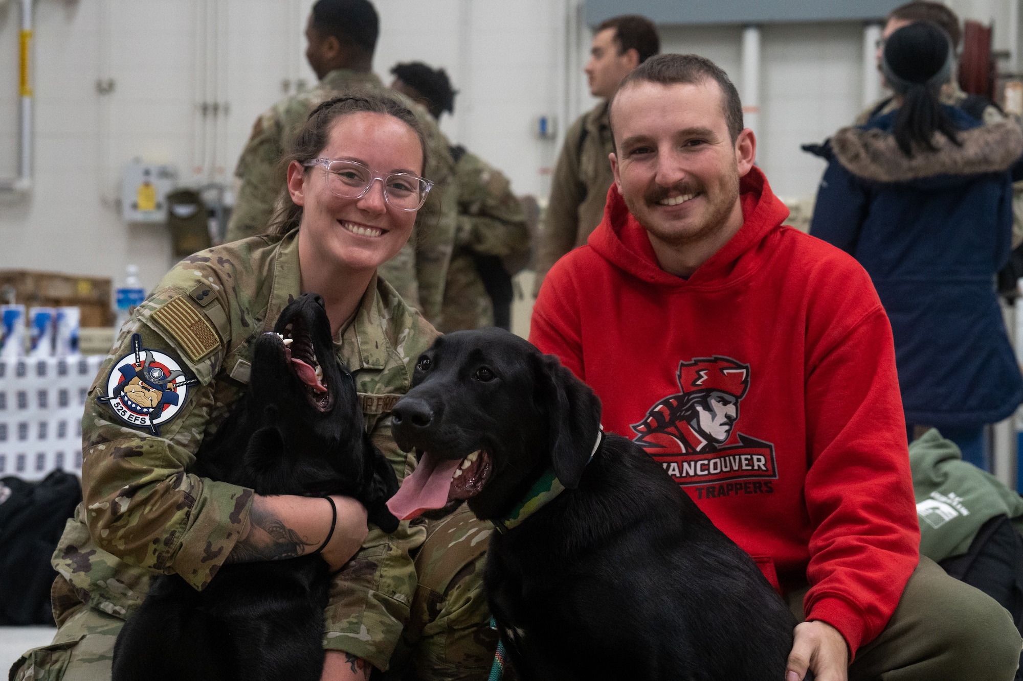 A U.S. Air Force Airman kneels next to her husband while holding her two dogs