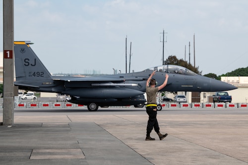 A U.S. Air Force crew chief assigned to the 336th Aircraft Maintenance Unit marshals an F-15E Strike Eagle onto the apron at Kadena Air Base, Japan, April 8, 2023. The Strike Eagles arrived from Seymour Johnson Air Force Base, North Carolina, to ensure continuous fighter presence through the phased return of Kadena’s fleet of F-15C/D Eagles to the United States. (U.S. Air Force photo by Senior Airman Jessi Roth)