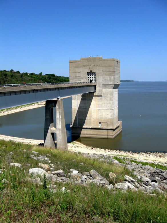 Tuttle Creek Dam can be seen in the water with a blue sky in the background and green grass in the foreground.