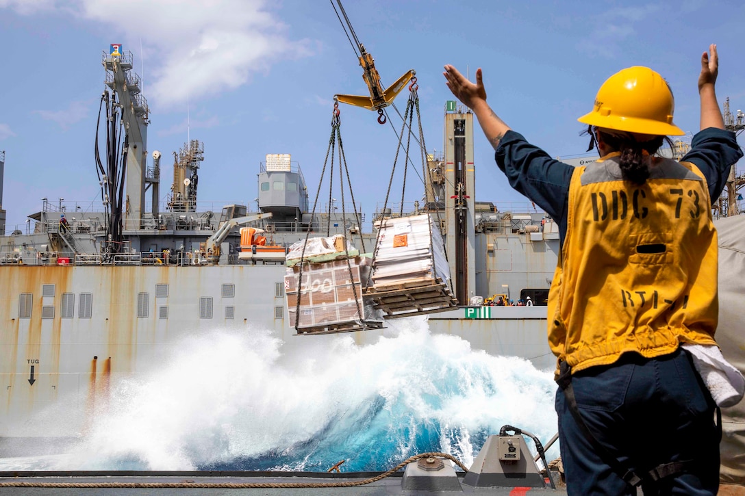 A sailor raises their arms toward a ship.