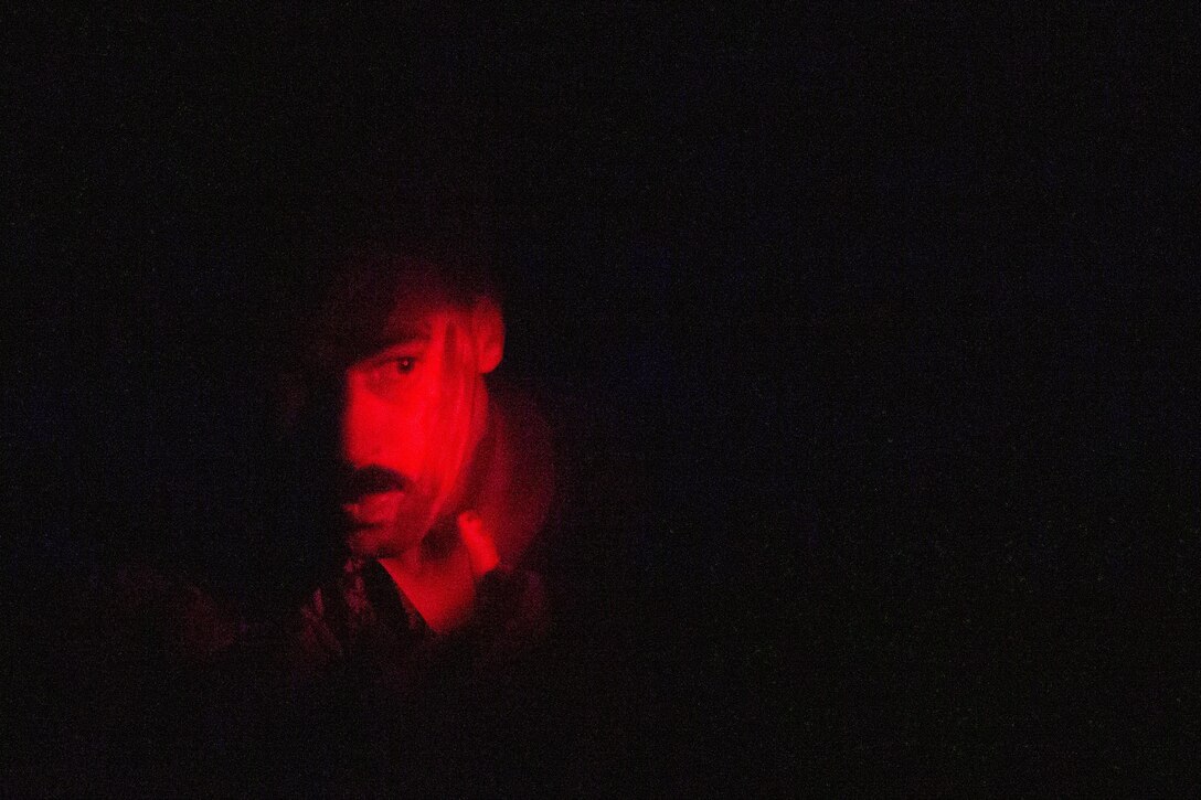 A Marine applies face paint in a dark area, illuminated by a red light.