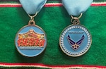 Fiesta Medal 2023 displayed on a green background. One side of the coin depicts the heritage of San Antonio. The opposite side depicts the Air Force Logo.