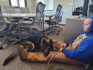 U.S. Air Force Staff Sgt. Nicholas Willet, 9th Security Forces Squadron K-9 handler, sits with Military Working Dog Gandy B-449.