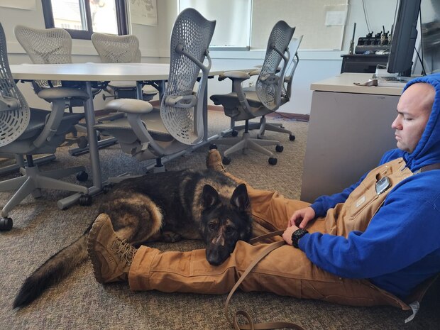 U.S. Air Force Staff Sgt. Nicholas Willet, 9th Security Forces Squadron K-9 handler, sits with Military Working Dog Gandy B-449.