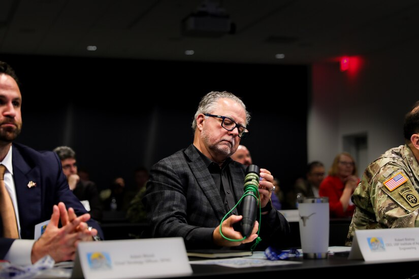 One man sitting at a table examines a 3D printed device.