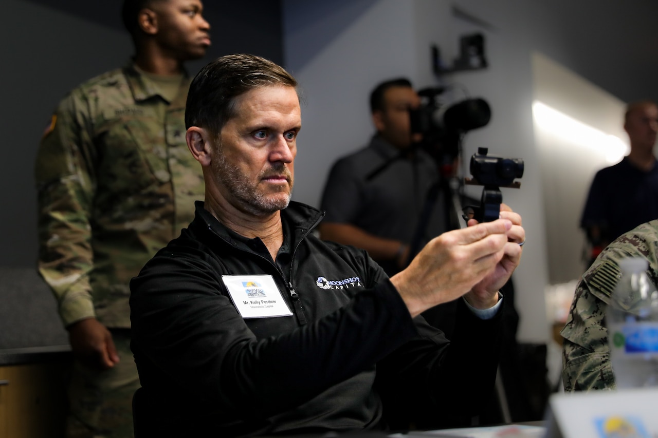 One man sitting at a table examines a 3D printed device.