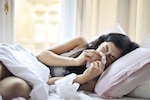 Woman lying on bed while blowing her nose