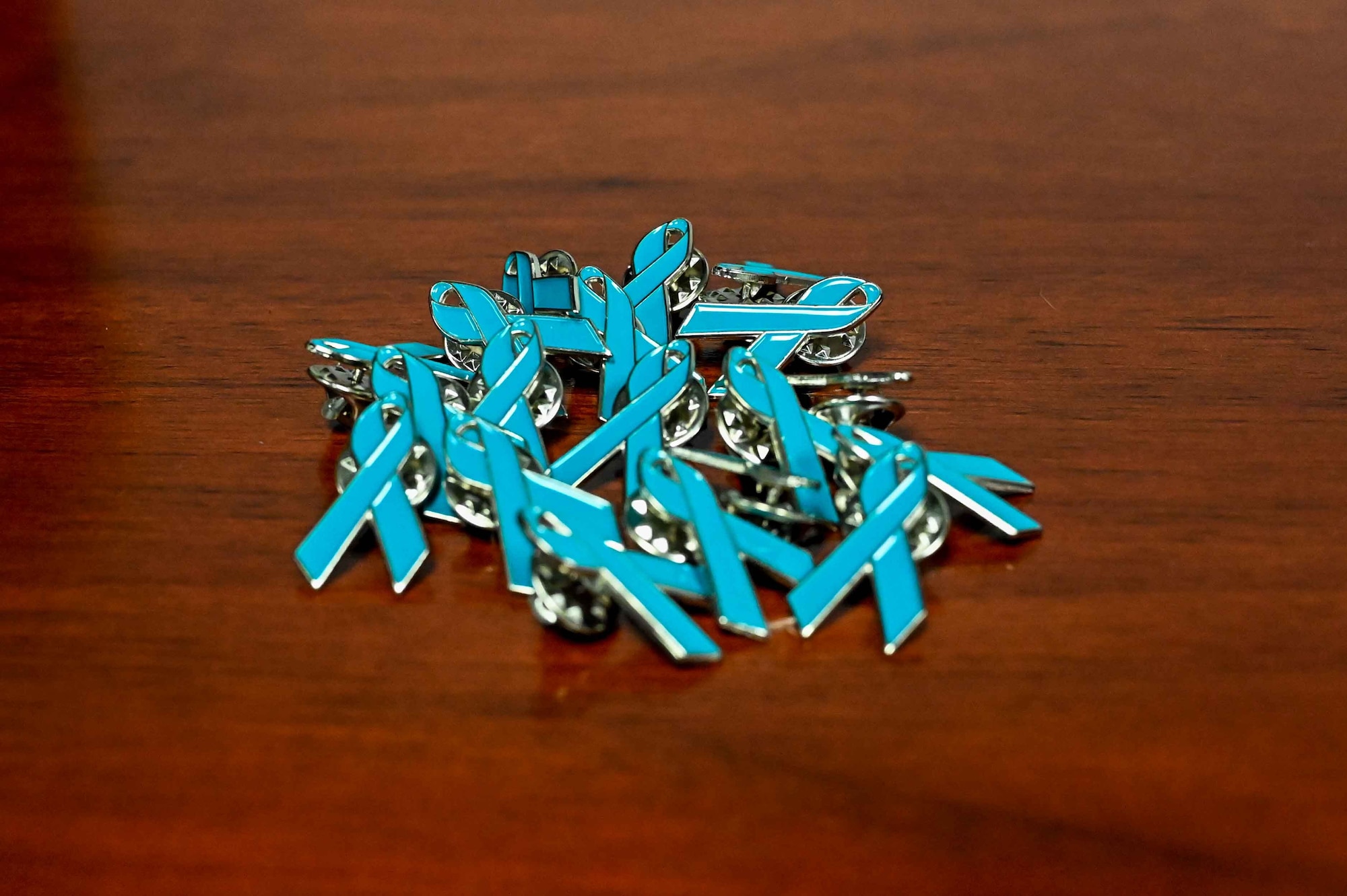 A pile of teal ribbons pins sit on a table at Altus Air Force Base (AFB), Oklahoma, April 4, 2023.Airmen on Altus AFB are encouraged to real the teal ribbon on their lapel every Tuesday during the month of April. (U.S. Air Force photo by Airman 1st Class Kari Degraffenreed)