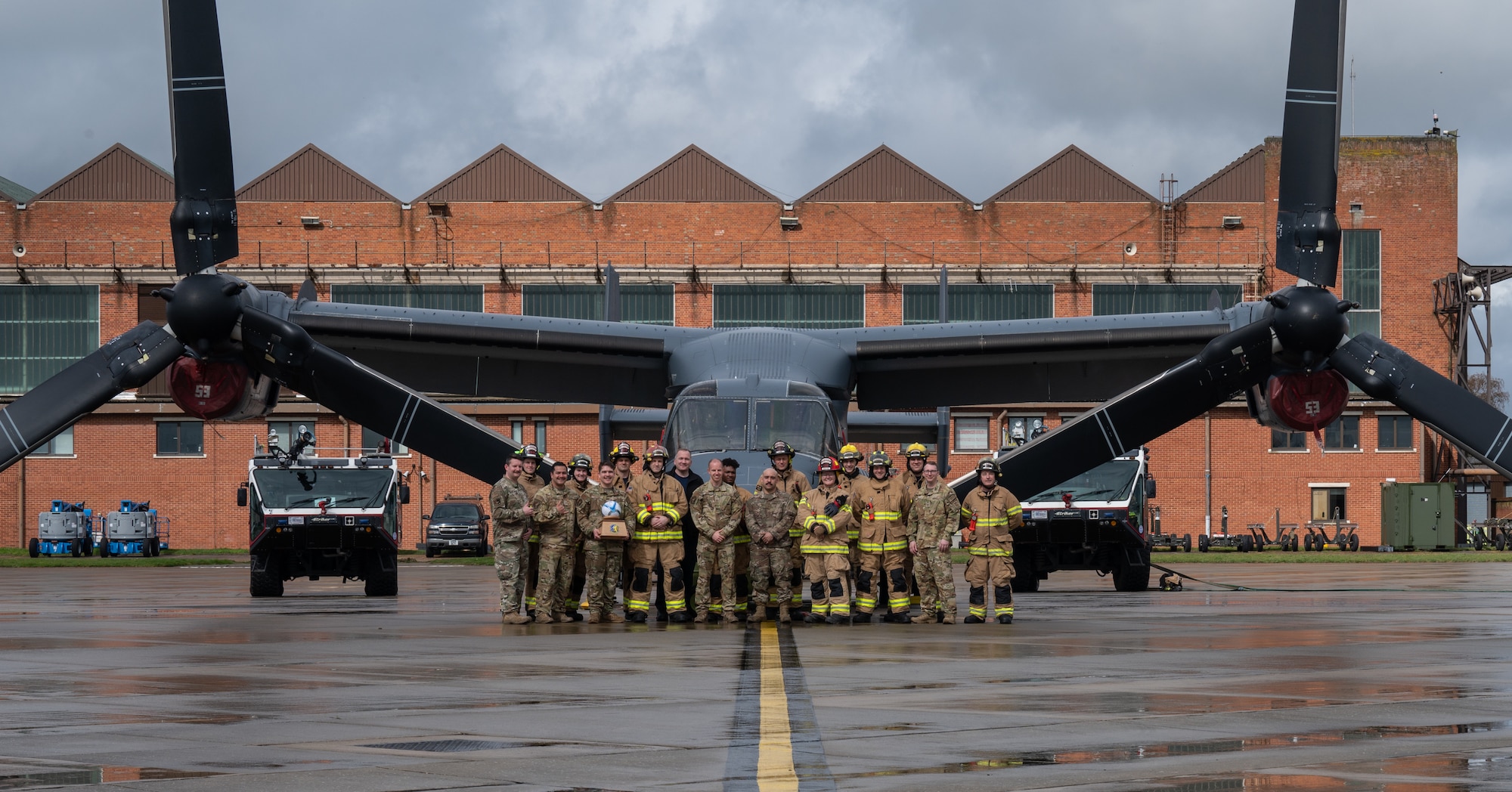 Personnel assigned to the 100th Air Refueling Wing and 352nd Special Operations Wing, stand in front of a CV-22B Osprey aircraft assigned to the 352nd SOW, after extinguishing a simulated fire, March 31, 2023, at Royal Air Force Mildenhall, England.