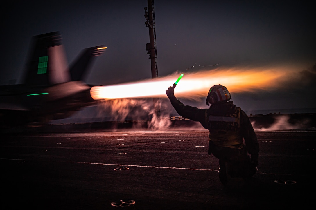 A fighter jet prepares to take off from an aircraft carrier at night.