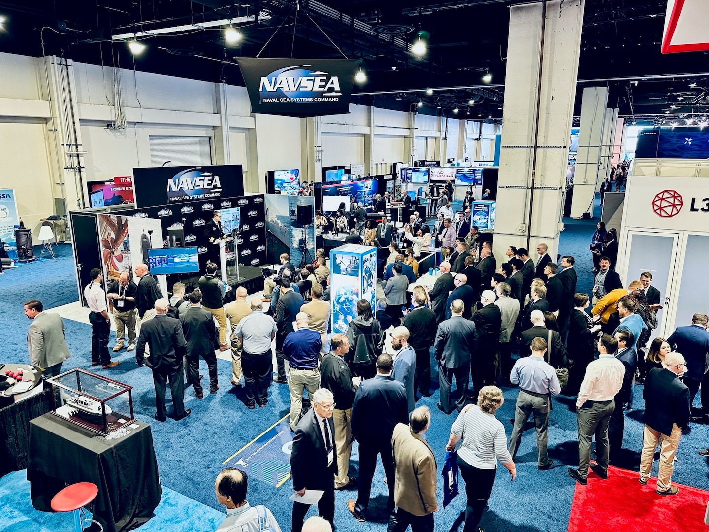 A crowd gathers around the Naval Sea Systems Command booth during the 2023 Sea-Air-Space Exposition in National Harbor, Md., on April 4, as Capt. Brian Metcalf, Program Manager, Gerald R. Ford-Class New Construction, gives a briefing on the future aircraft carriers program update. (U.S. Navy photo by Monica McCoy