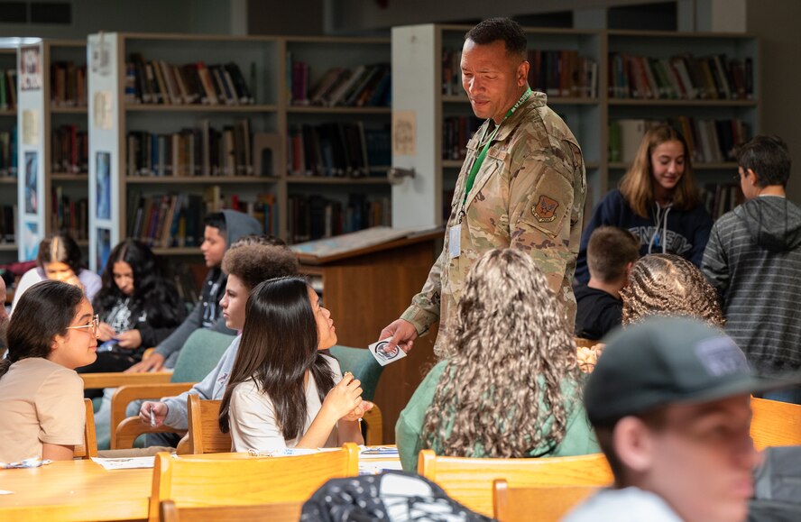 A male Airman hands out stickers to teens in a library