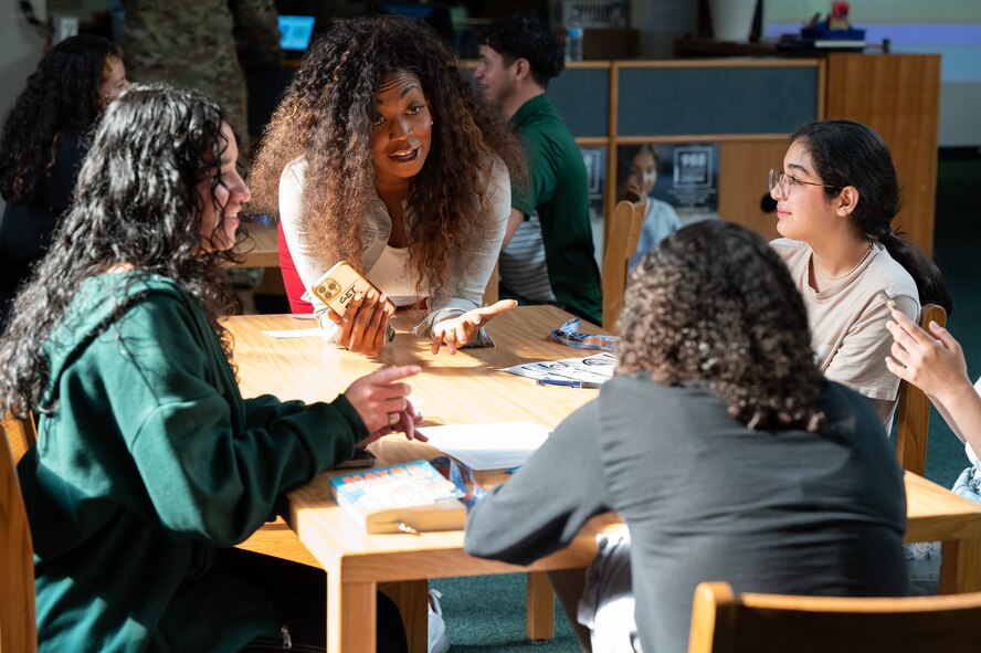 A woman leans over on a desk in a library and engages in conversation with teens