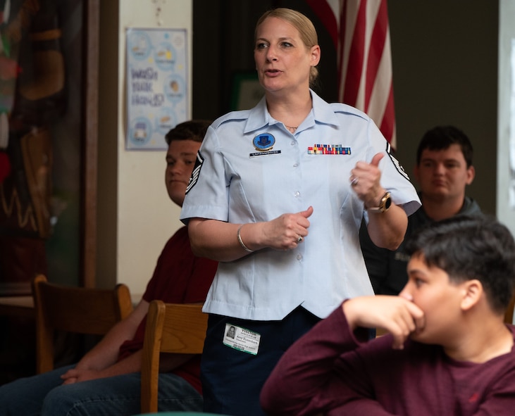 Female Air Force recruiter stands in a library while she speaks to teens around her