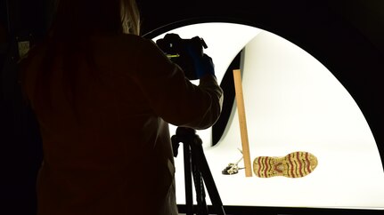 Forensic Scientist examining and taking pictures of footwear evidence in a light box, in the lab