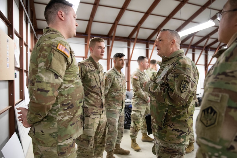 A group of Soldiers standing in a warehouse having a conversation.