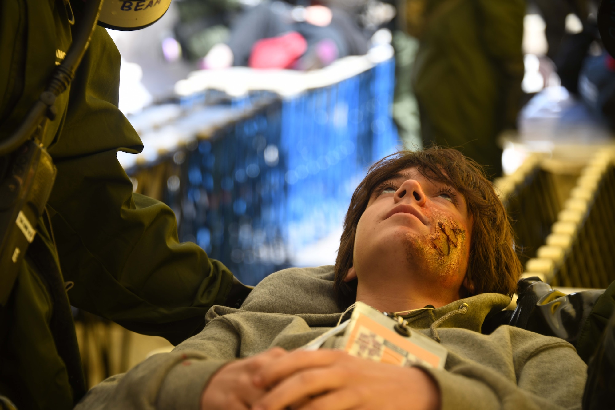 An actor with moulage laying on a stretcher looks up
