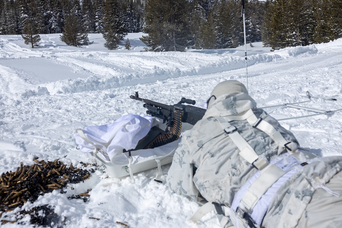 A US Marine fires an M240B machine gun across the snowy terrain