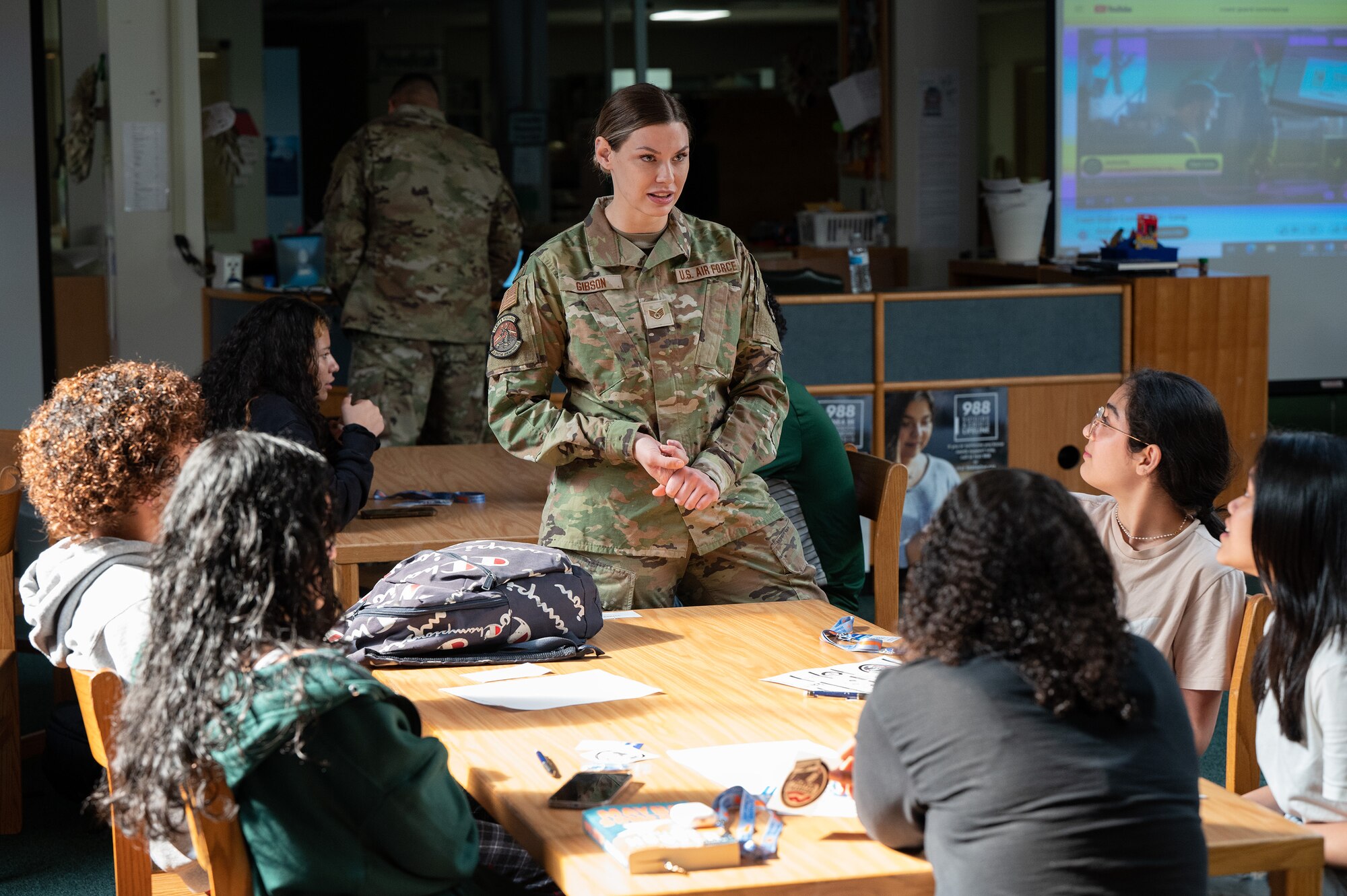 Female Airman talks to teens at a table in the school library