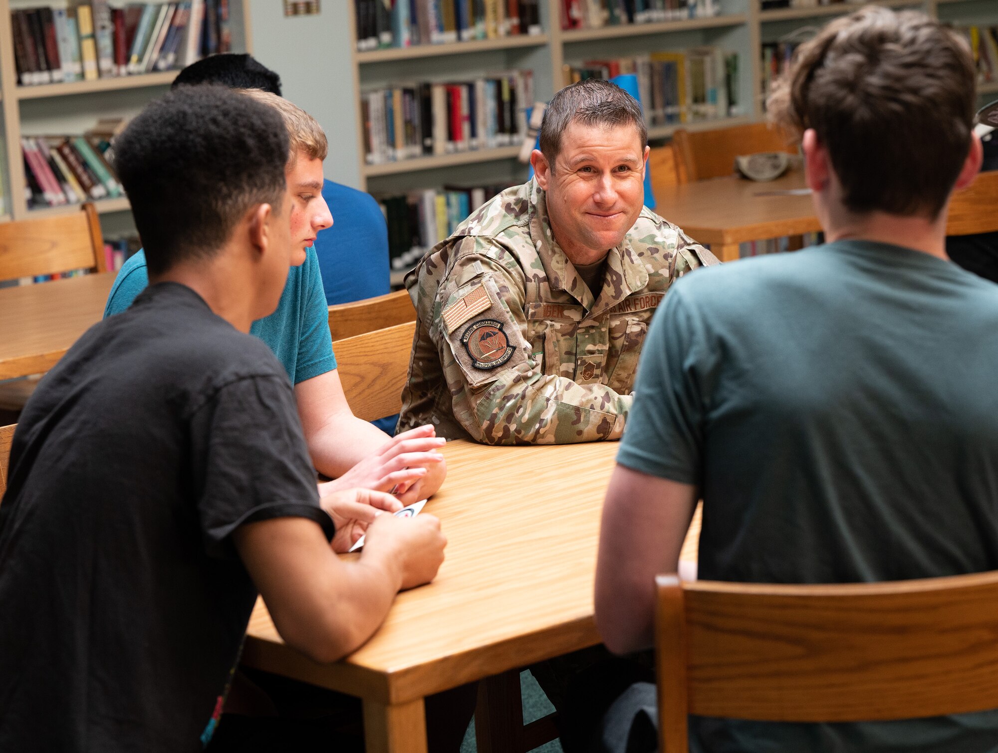 A male airman sits at a table in a library with teens