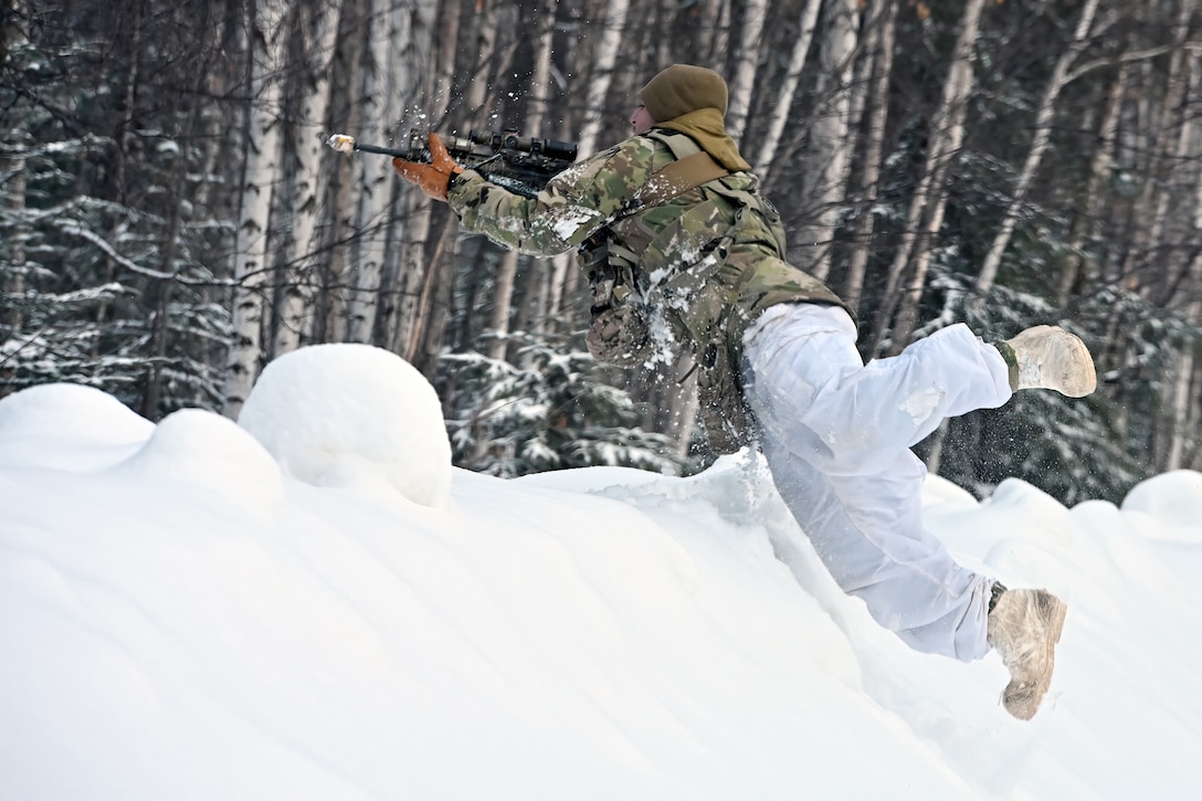 A soldier jumps on top of a large mound of snow.