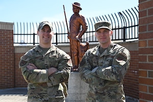 Two uniform Airmen pose for a photo outside with the Minuteman statue in the background.