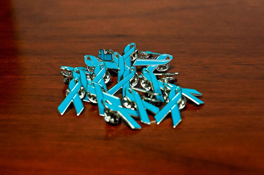Teal ribbon lapel pins sit in a pile on a table.