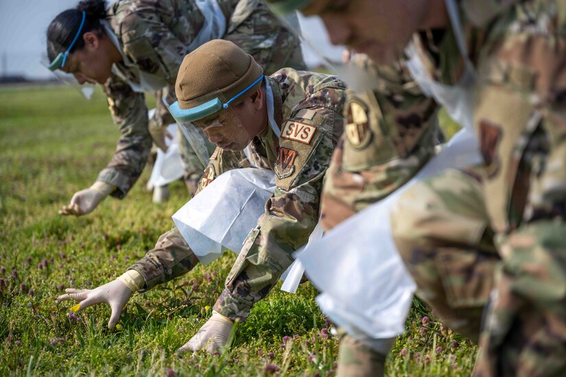 Airmen scour the ground on their hands and knees during a simulated plane crash exercise.
