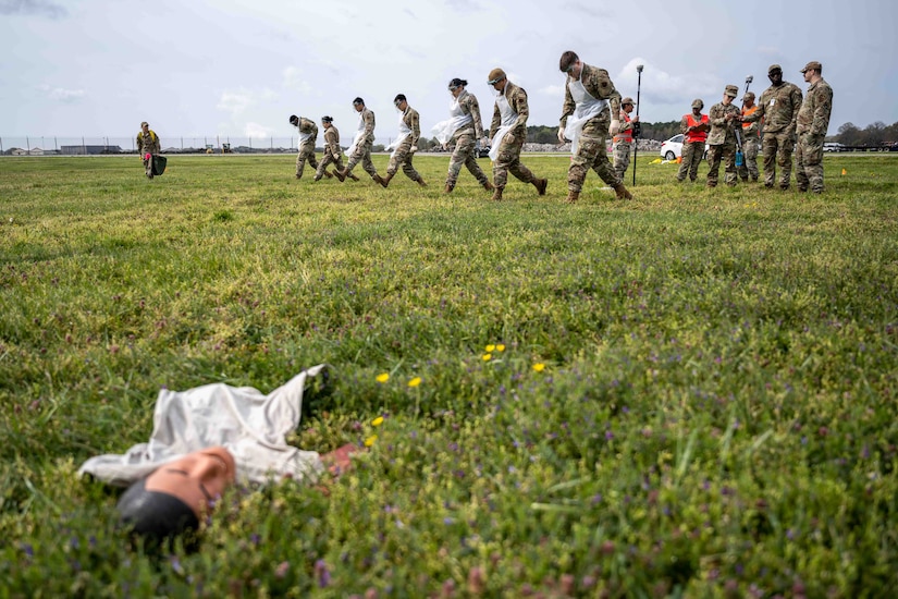 Airmen search the ground in the background while a mannequin simulating a plane crash victim lies in the foreground.