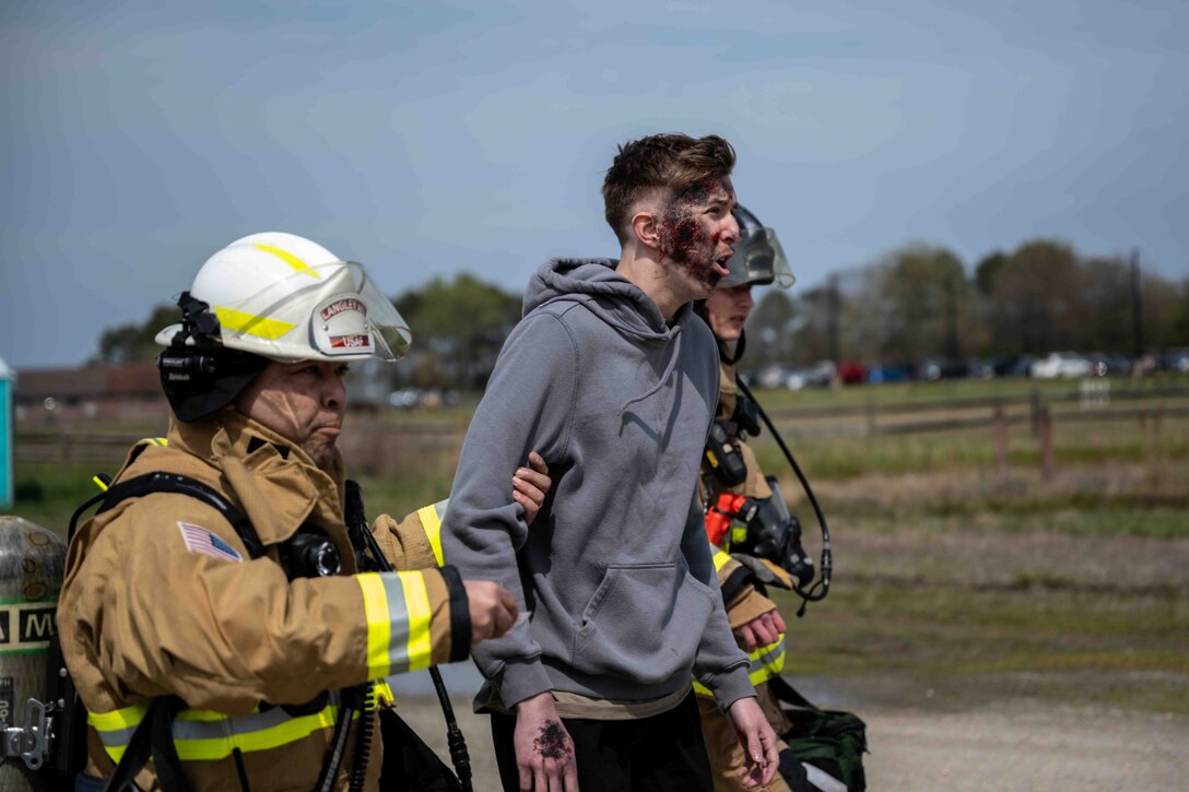 Firefighters help a simulated-victim walk to medical aid during an exercise