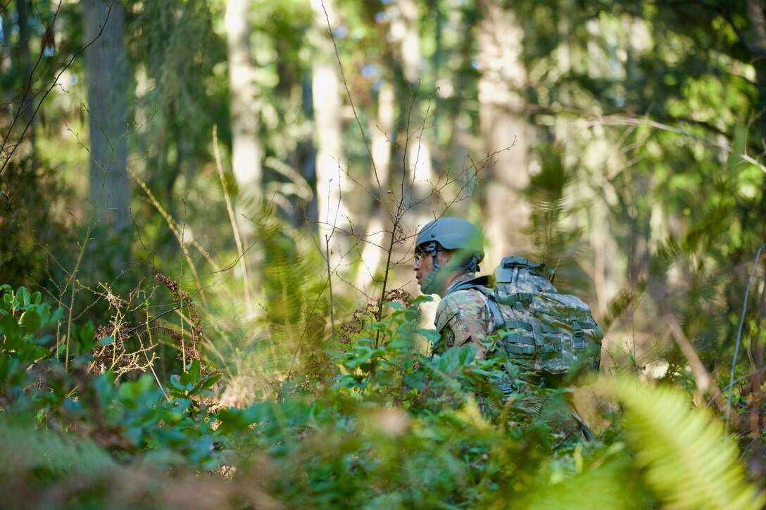 A Soldier walking in the forest with a helmet, eye production, and rucksack.