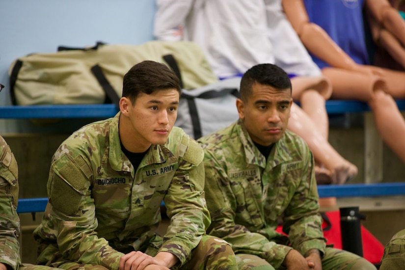 Two Soldiers sitting on bleachers indoors.