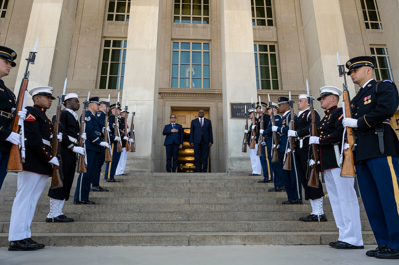 Secretary of Defense Lloyd J. Austin III and another leader stand at top of Pentagon steps, flanked by honor guardsmen.