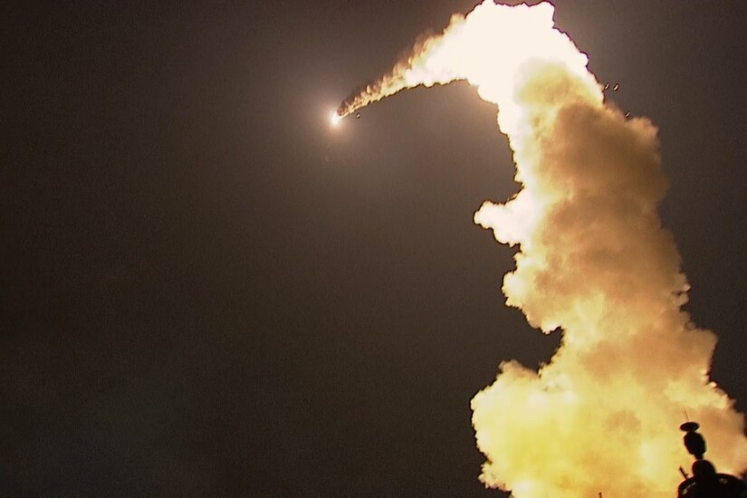 Smoke from the trail of a missile lights up a dark sky.