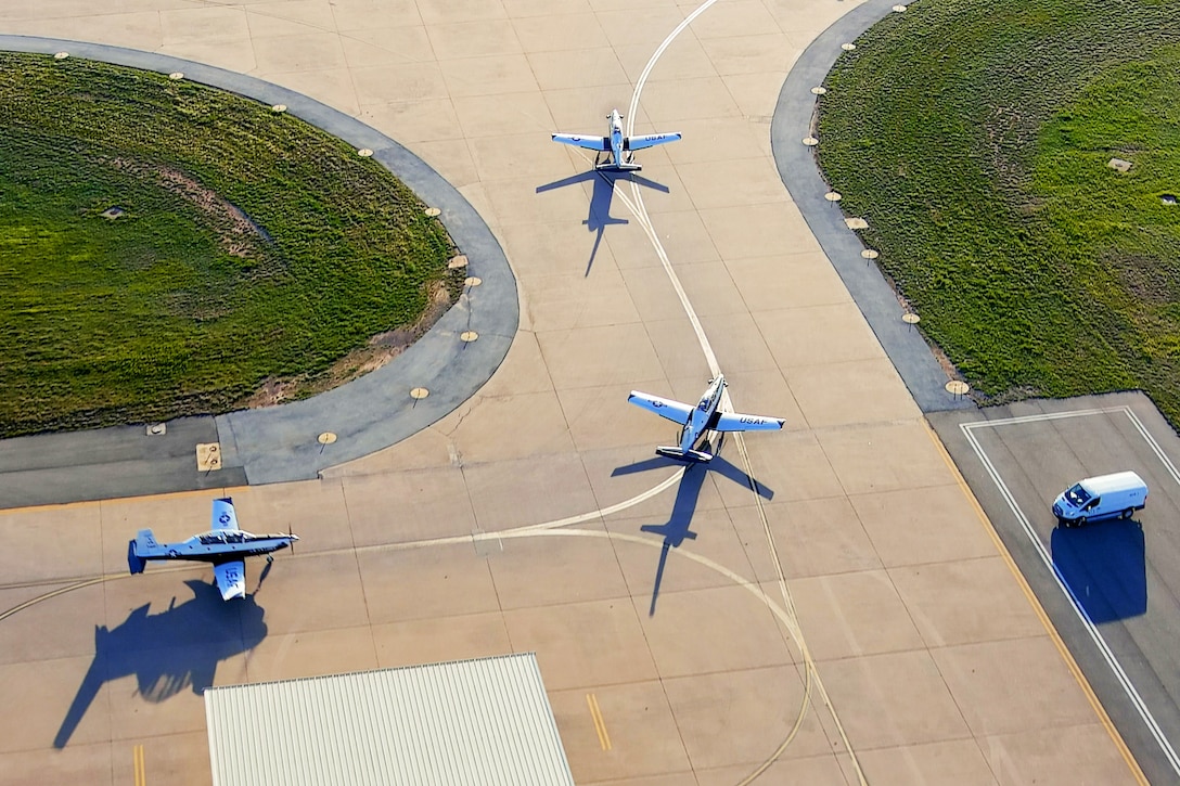 Three small planes line up on a runway.