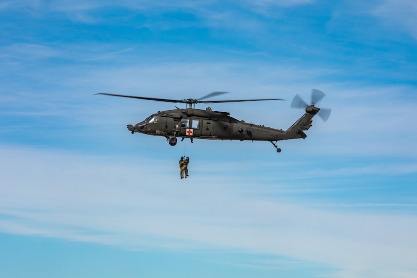 Soldiers hang in the air from a helicopter.