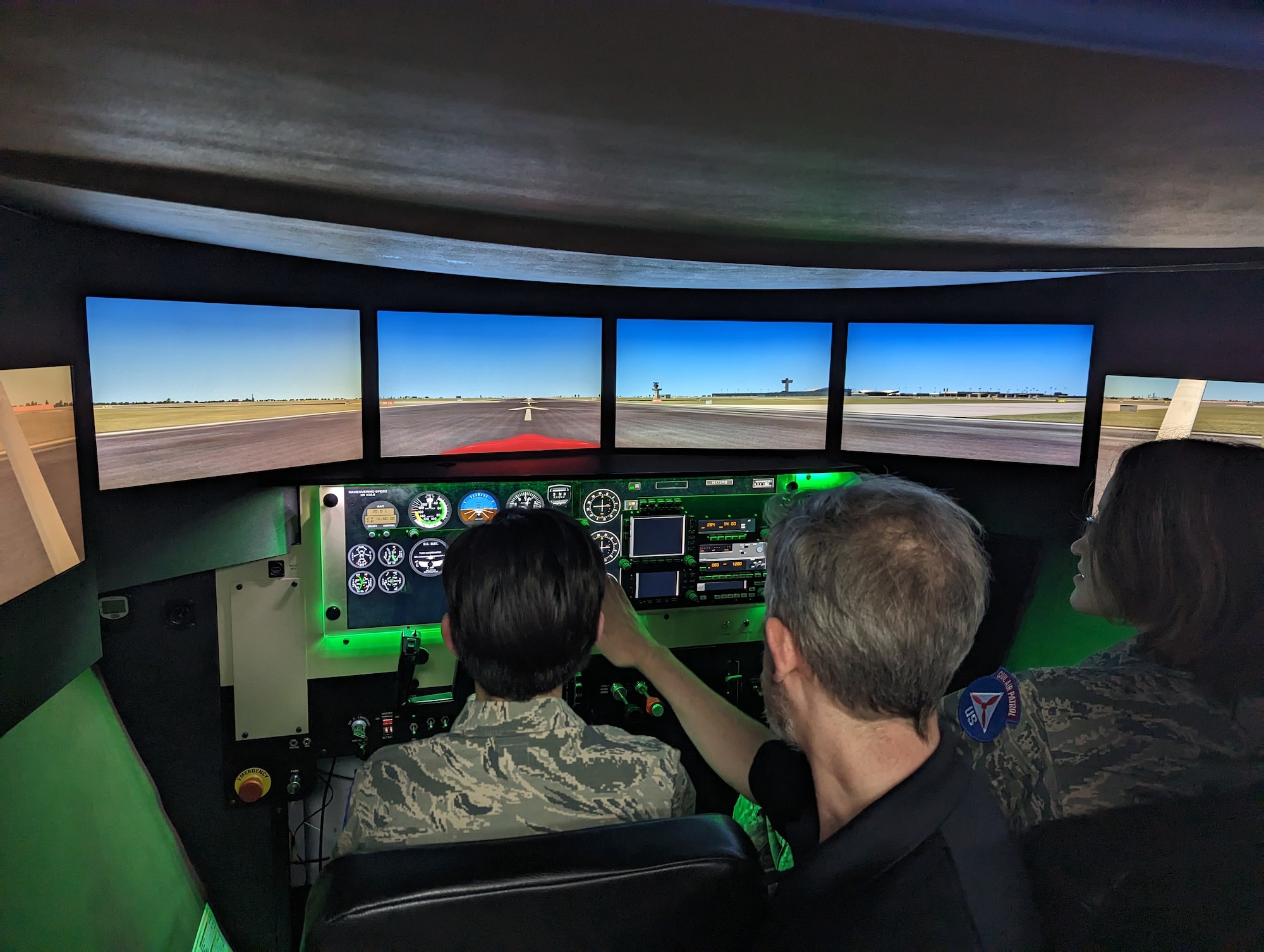 A flight instructor points at controls that two uniformed kids are operating a airplane simulator