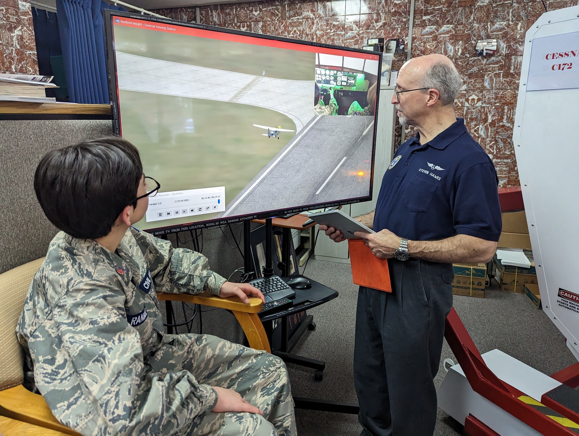 a seated cadet watches a screen as a standing adult points at it