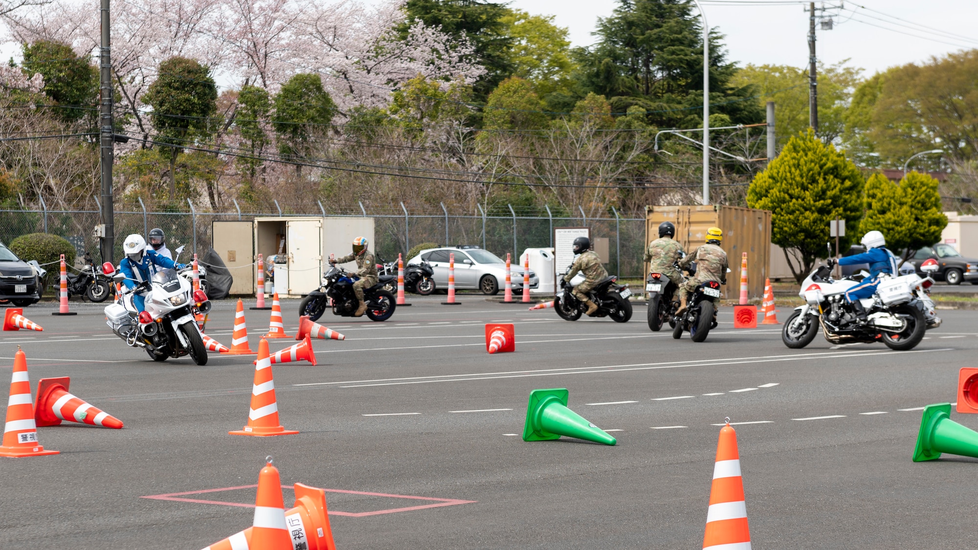 Several motorcycle riders weave through a path of cones in a parking lot