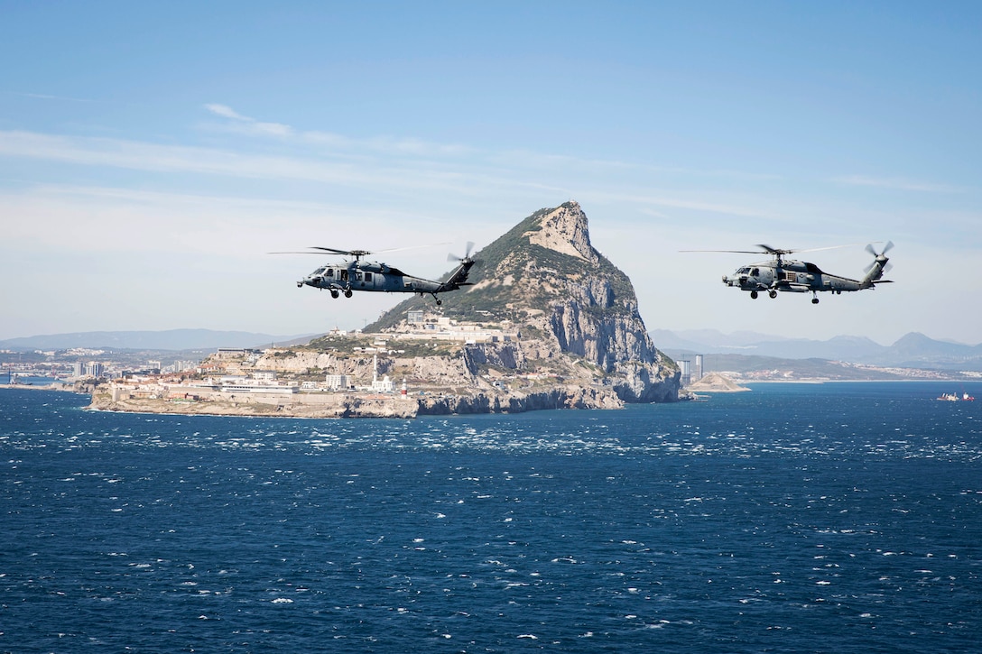 Two helicopters fly in formation at sea.