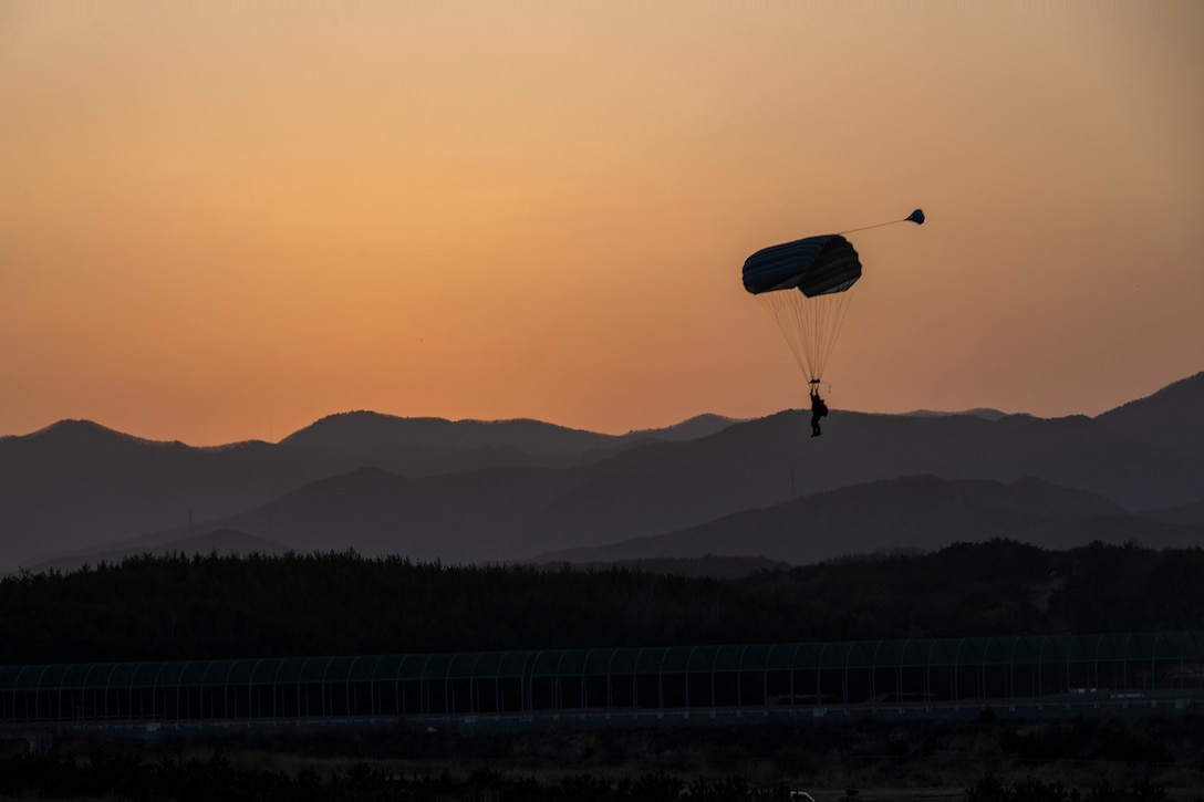 Silhouette of a Marine parachuting near a mountainous area.