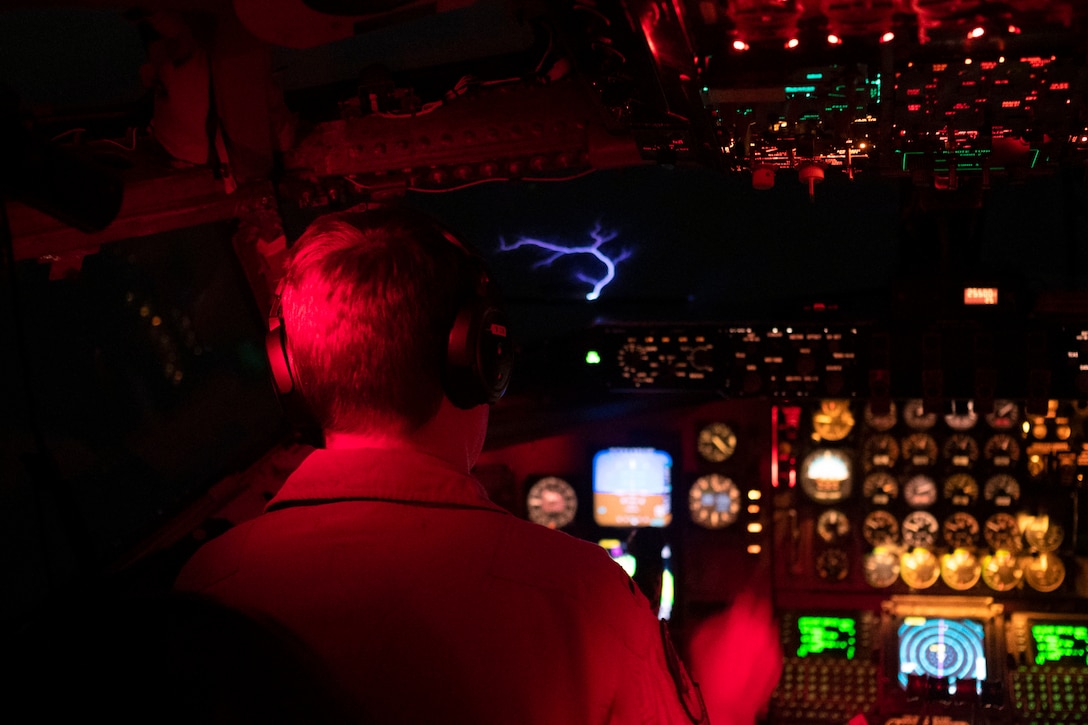 A blue lightning-like flash appears in the windshield of an illuminated cockpit as a pilot flies at night.