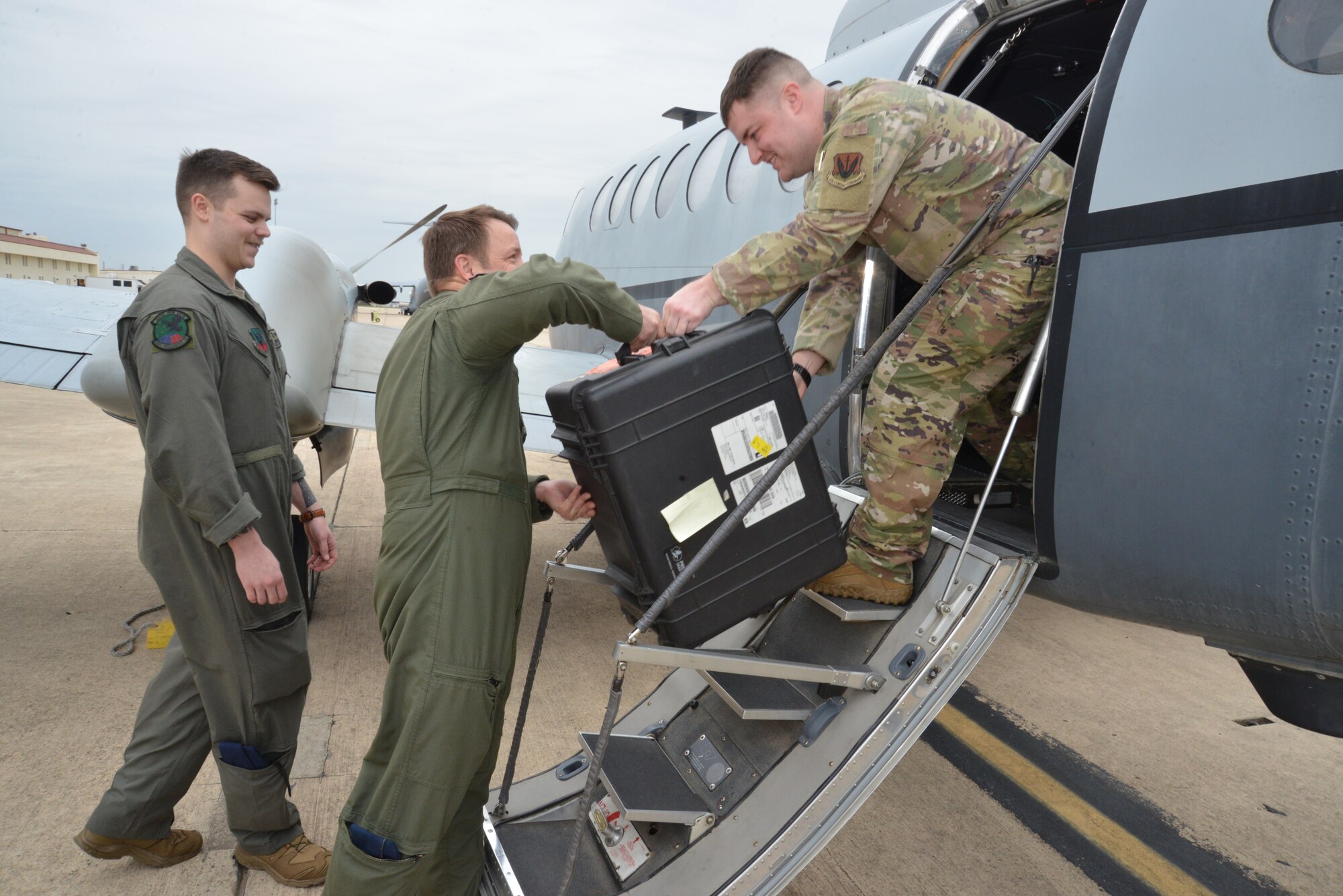 Lt. Col. Robby Trest, (middle) MC-12W Evaluator Pilot, from the 185th Special Operations Squadron, hands the Nebula, a specialized device used by tactical support operators, to Staff Sgt. Cole Weiss, tactical systems operator instructor, 306th Intelligence Squadron, as Staff Sgt. Gabriel Gibson, TSO instructor, 306th IS, stands ready to assist March 29, 2023, at Joint Base San Antonio-Lackland, Texas. The MC-12W Liberty aircrew from Will Rogers Air National Guard Base, Oklahoma City, were there to pick up the Nebula from an MC-12W that crashed April 27, 2013, near Kandahar Airfield, Afghanistan.
