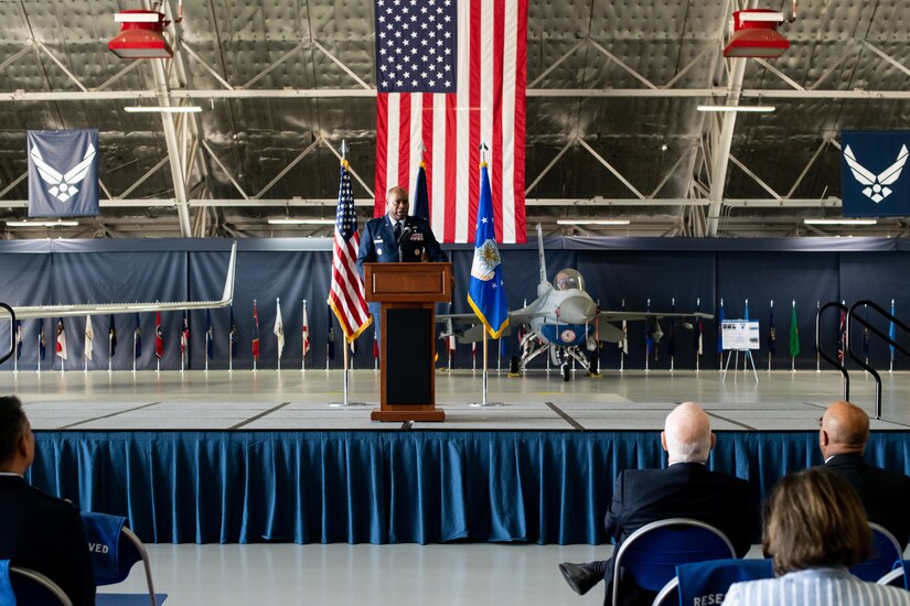 A military member speaks at a lectern in front of a U.S. flag.