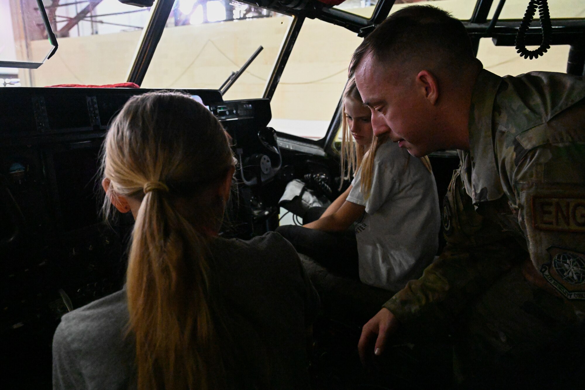 man in uniform demonstrates controls of an aircraft to children