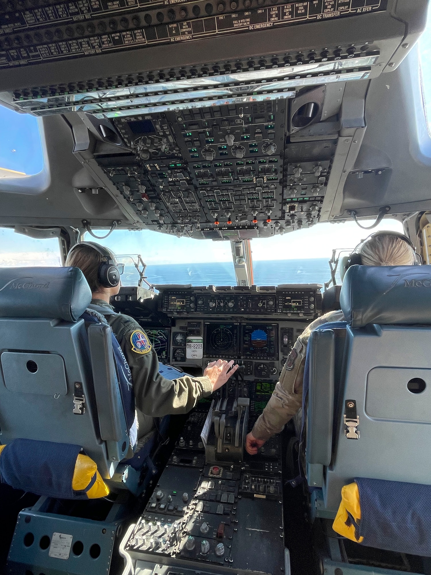 Pictured taken from behind as two female pilots fly a C-17 Globemaster over the ocean at a low level.