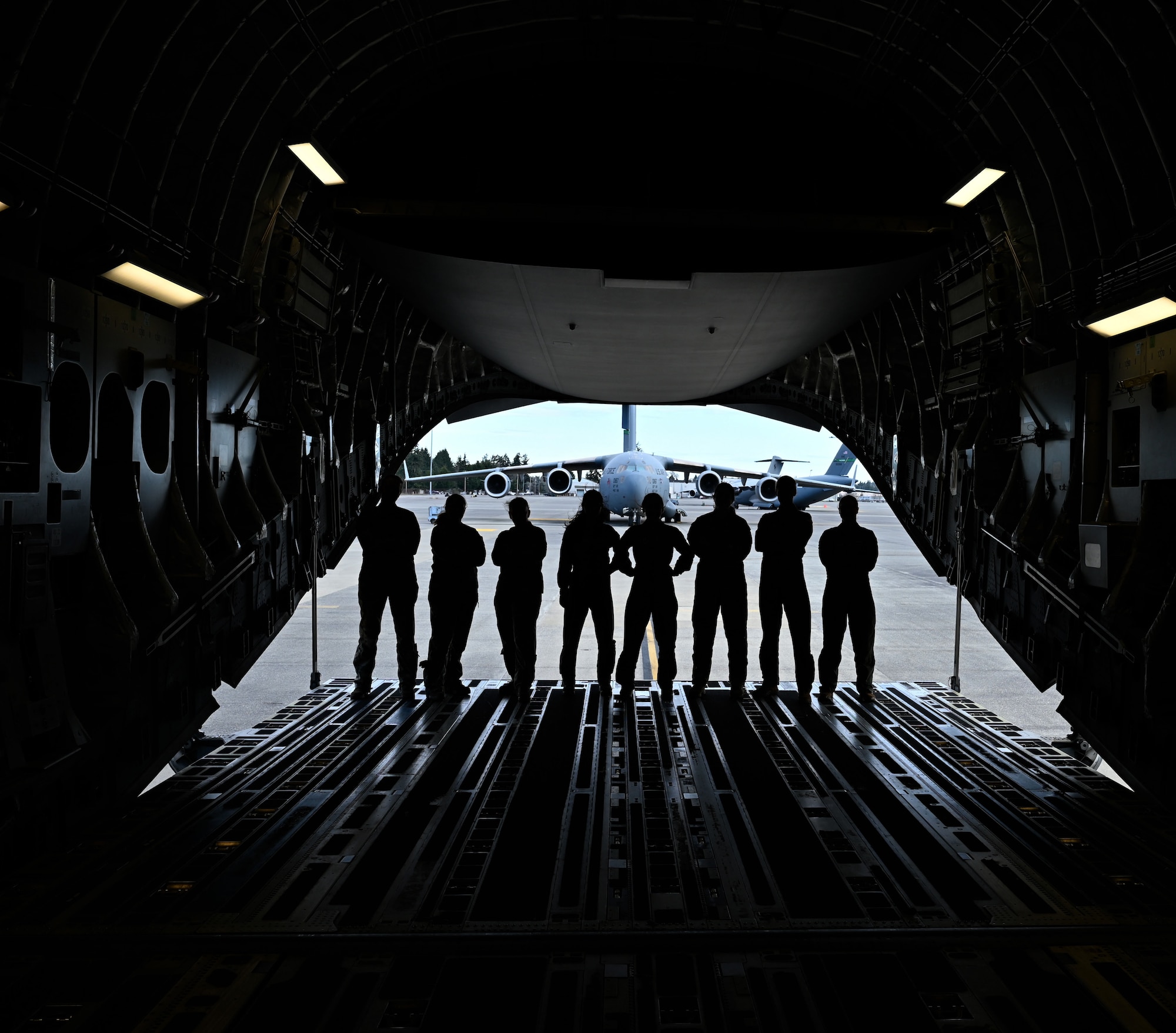 A group of 8 female pilots and loadmasters pose on the ramp of a C-17 Globemaster as it is parked in front of another C-17.